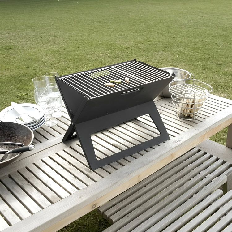 A black foldable charcoal BBQ grill on a wooden picnic table with food and drinks 48-31