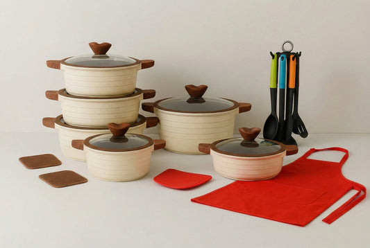 Set of ceramic cookware with lids, spatulas, and a red apron on a light background