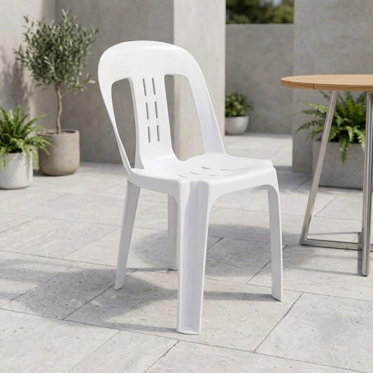 A white plastic outdoor dining chair with a slatted back and seat, shown on a light stone patio next to a wooden table.